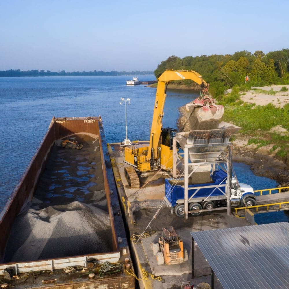Backhoe unloading dirt from a barge into a dumptruck